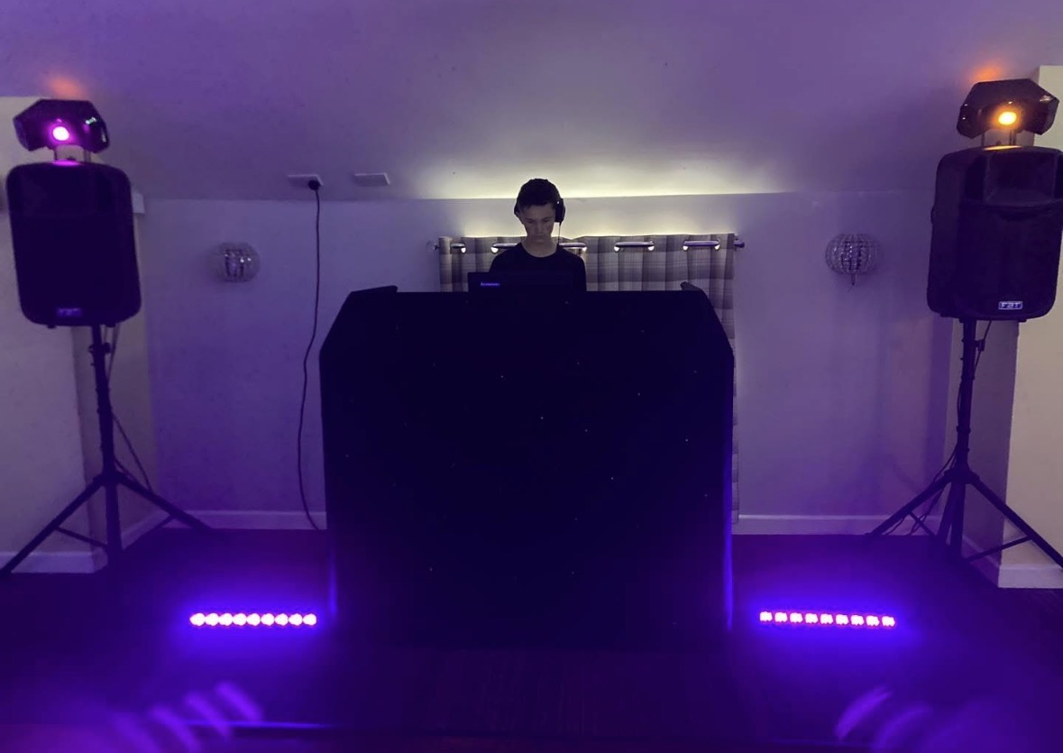DJ performing behind a starlit booth with purple uplighting